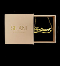 Load image into Gallery viewer, Gold custom name necklace with “Fatima” in cursive script, displayed inside a beige Silani jewelry box with gold foil branding on a black background.