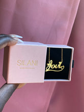 Load image into Gallery viewer, Gold custom name necklace with the name “Jovi” displayed in a pink Silani jewelry box, held against a blush pink background.